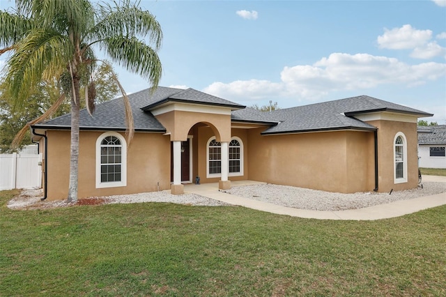 view of front facade with a shingled roof, fence, a front lawn, and stucco siding