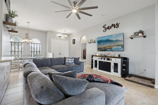 living area featuring light tile patterned floors, baseboards, arched walkways, and ceiling fan with notable chandelier