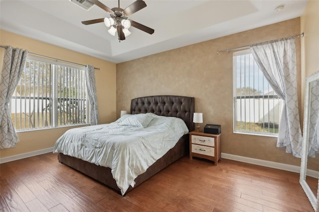 bedroom with a tray ceiling, hardwood / wood-style flooring, visible vents, and baseboards