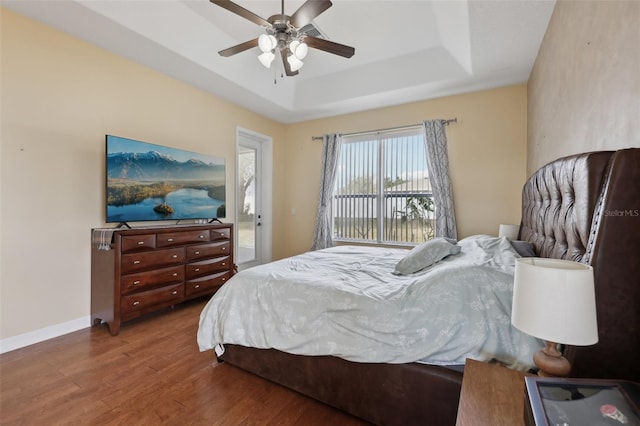 bedroom with baseboards, ceiling fan, wood finished floors, access to exterior, and a tray ceiling