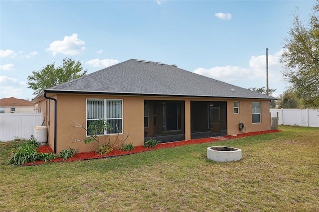 rear view of property featuring a yard, fence, a fire pit, and stucco siding