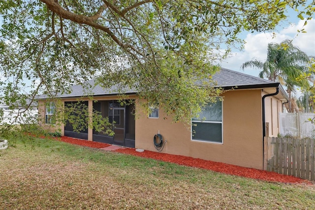 rear view of property with a shingled roof, fence, a sunroom, a lawn, and stucco siding