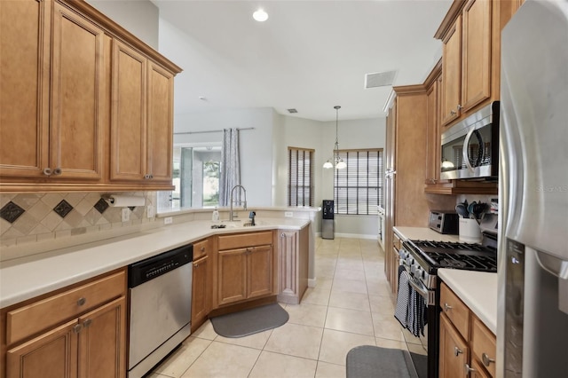 kitchen with stainless steel appliances, a peninsula, a sink, backsplash, and brown cabinetry