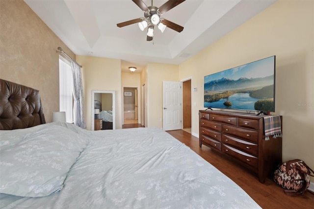 bedroom featuring ensuite bathroom, a tray ceiling, dark wood finished floors, and a ceiling fan