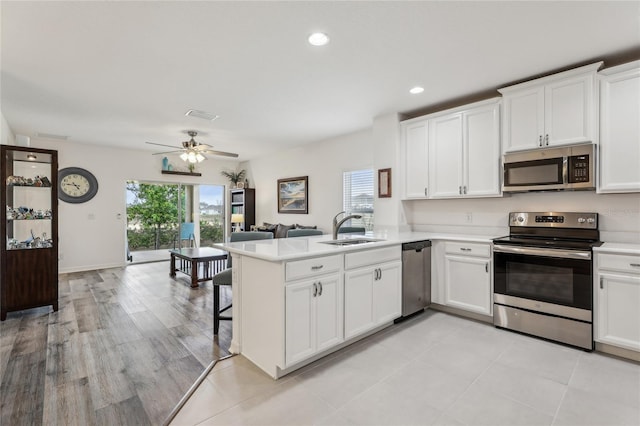 kitchen featuring a sink, open floor plan, stainless steel appliances, a peninsula, and light countertops