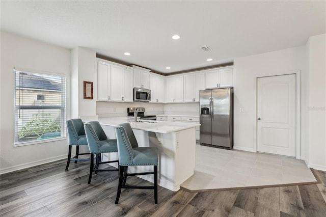 kitchen featuring light countertops, a kitchen bar, appliances with stainless steel finishes, a peninsula, and white cabinetry