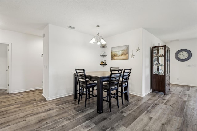 dining area featuring wood finished floors, visible vents, baseboards, a textured ceiling, and a notable chandelier