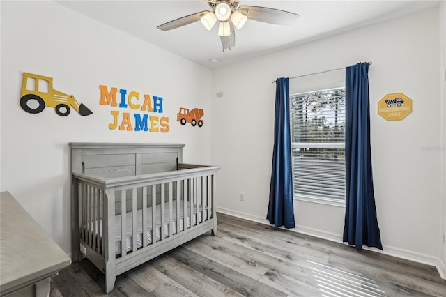 bedroom featuring ceiling fan, baseboards, a nursery area, and wood finished floors