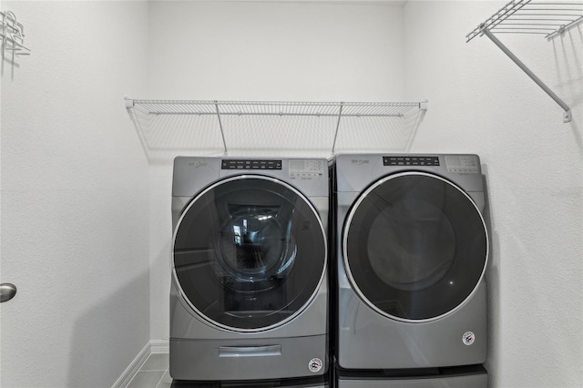 washroom featuring washing machine and clothes dryer, laundry area, tile patterned flooring, and baseboards