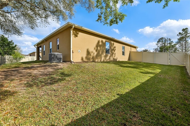 rear view of house with a yard, central AC unit, a fenced backyard, and stucco siding