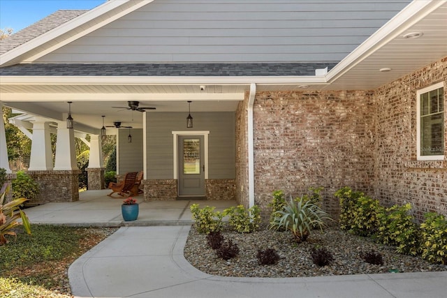 entrance to property with covered porch, a ceiling fan, brick siding, and roof with shingles