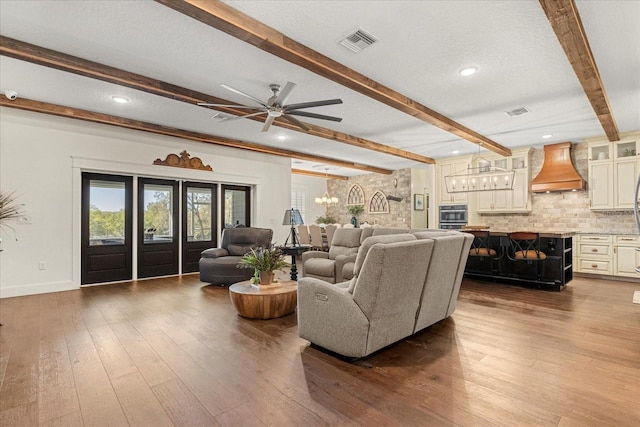 living room with a textured ceiling, hardwood / wood-style flooring, beamed ceiling, visible vents, and a ceiling fan