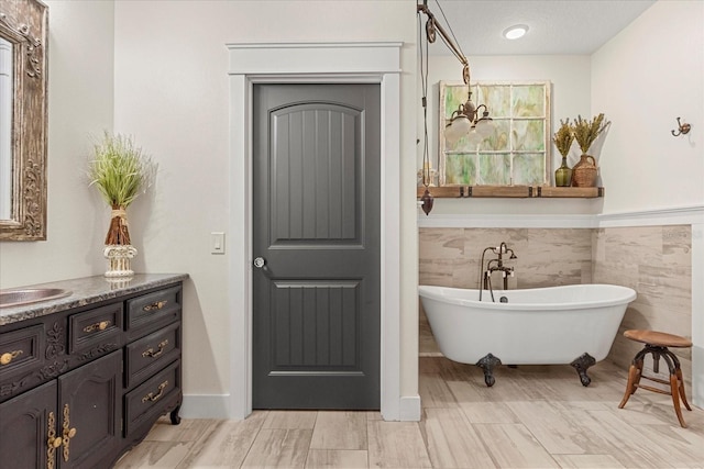 full bathroom with tile walls, wainscoting, vanity, and a freestanding bath