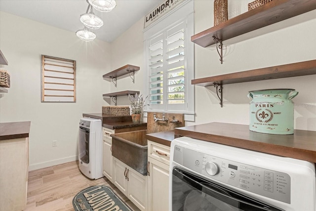 kitchen with open shelves, baseboards, a sink, dark countertops, and light wood finished floors