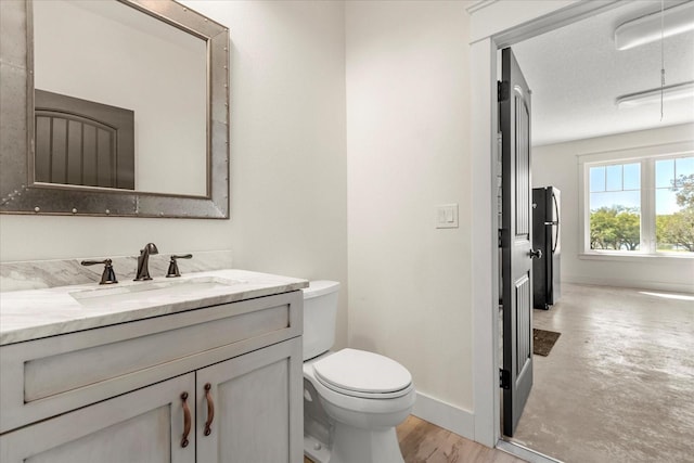 bathroom with a textured ceiling, baseboards, toilet, wood finished floors, and vanity