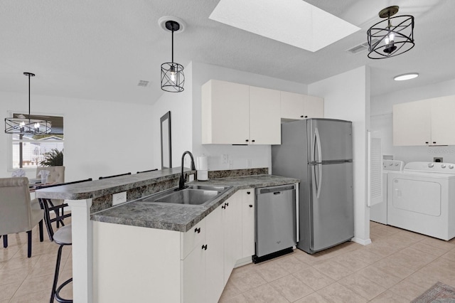 kitchen with dark countertops, independent washer and dryer, a peninsula, stainless steel appliances, and a sink