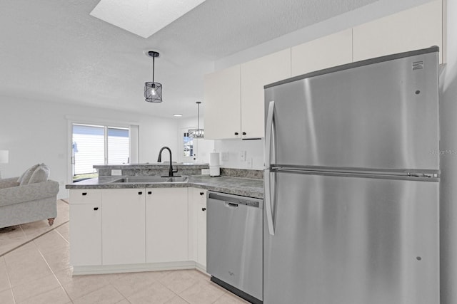 kitchen featuring light tile patterned floors, dark countertops, appliances with stainless steel finishes, a peninsula, and a sink