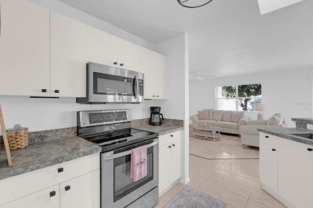 kitchen with appliances with stainless steel finishes, open floor plan, a textured ceiling, white cabinetry, and light tile patterned flooring