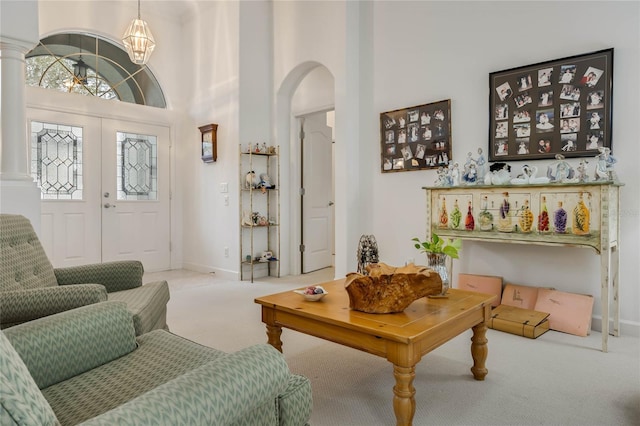 living area featuring carpet floors, arched walkways, decorative columns, and a high ceiling