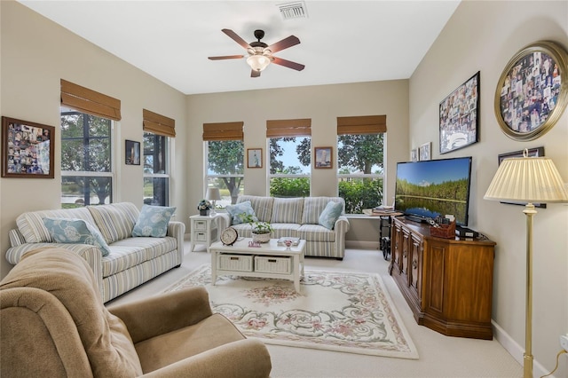 living area with ceiling fan, a wealth of natural light, visible vents, and light colored carpet