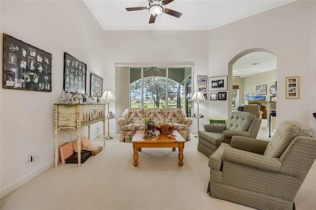 living room featuring arched walkways, baseboards, a ceiling fan, ornamental molding, and carpet