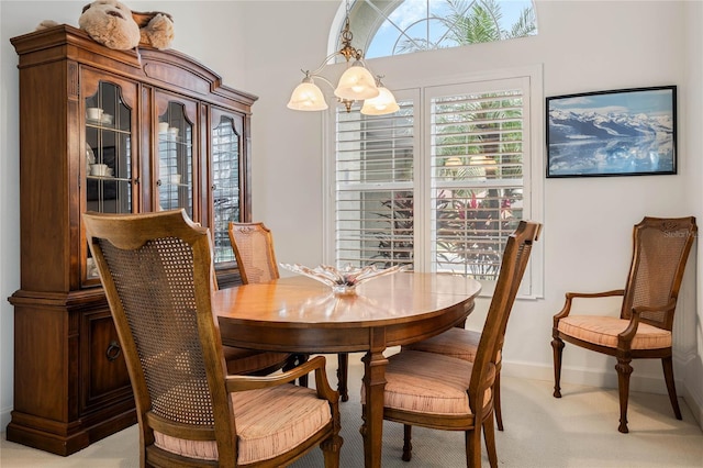 dining room featuring light carpet, baseboards, and a notable chandelier