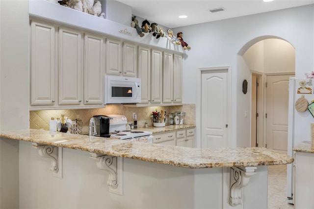 kitchen with white appliances, light stone counters, decorative backsplash, and a breakfast bar area