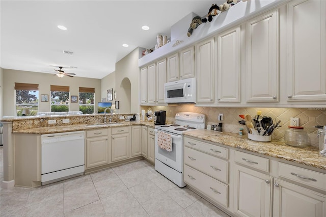 kitchen with light stone counters, tasteful backsplash, a sink, white appliances, and a peninsula