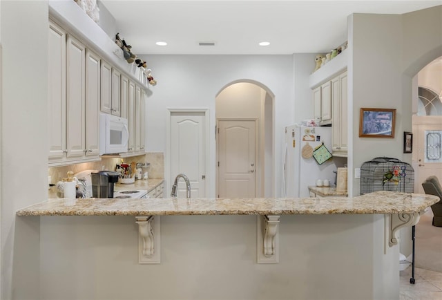 kitchen featuring a breakfast bar area, white appliances, a sink, visible vents, and decorative backsplash