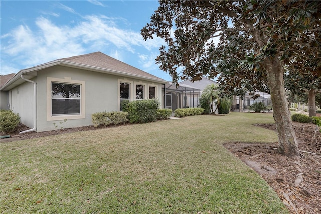 back of property with stucco siding, a shingled roof, glass enclosure, and a yard