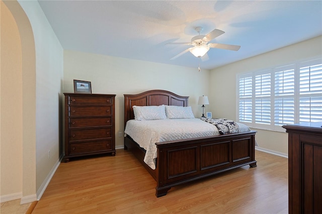 bedroom with baseboards, arched walkways, light wood finished floors, and a ceiling fan