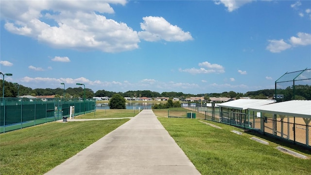 view of community featuring fence, a water view, and a lawn