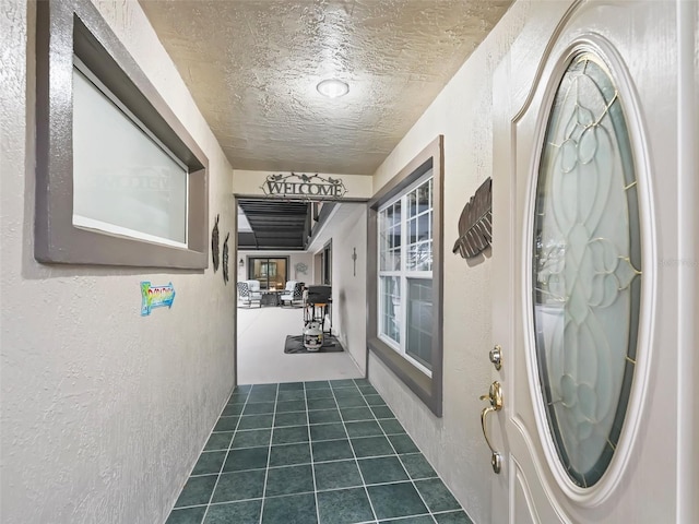 foyer entrance with a textured ceiling, a textured wall, and dark tile patterned floors