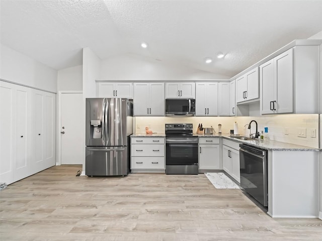 kitchen with lofted ceiling, light wood-style flooring, appliances with stainless steel finishes, a sink, and backsplash