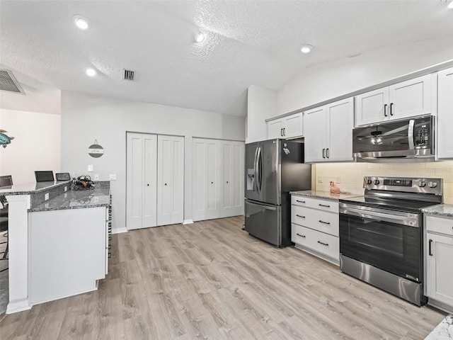 kitchen with stone counters, stainless steel appliances, white cabinetry, vaulted ceiling, and a kitchen bar