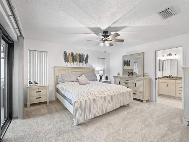 bedroom with light colored carpet, visible vents, connected bathroom, and a textured ceiling