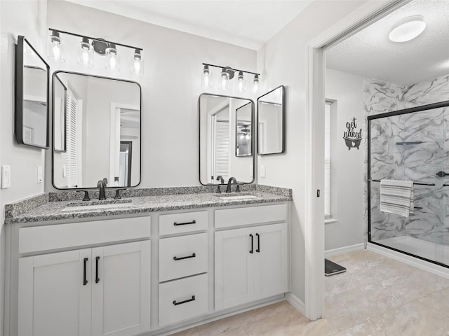 bathroom with a sink, a textured ceiling, a marble finish shower, and double vanity