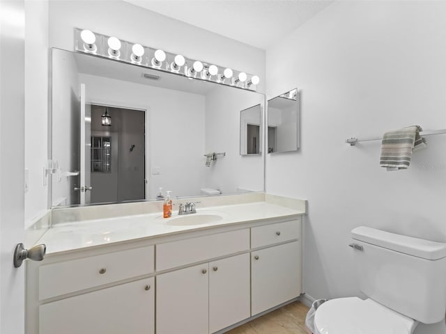 half bathroom with toilet, visible vents, vanity, and baseboards