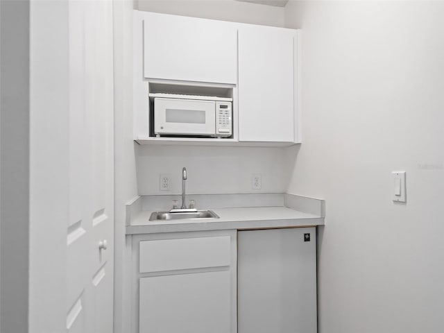 kitchen with white microwave, modern cabinets, light countertops, white cabinetry, and a sink