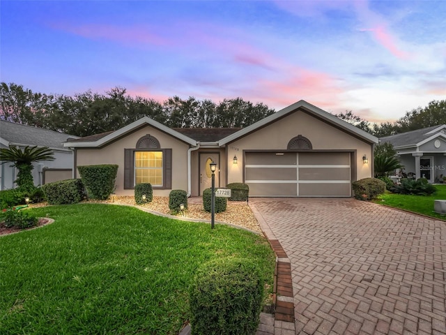 ranch-style house with a garage, a yard, decorative driveway, and stucco siding