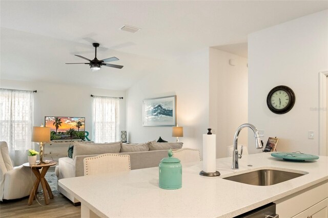 kitchen with a ceiling fan, a sink, vaulted ceiling, white cabinets, and open floor plan