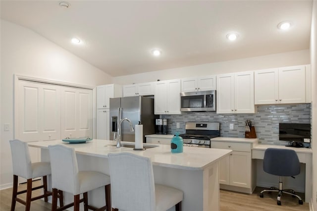 kitchen featuring a breakfast bar, a sink, tasteful backsplash, stainless steel appliances, and lofted ceiling