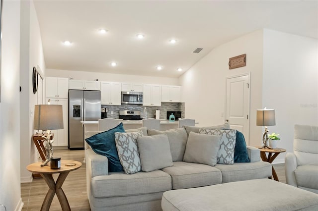 living room with lofted ceiling, recessed lighting, visible vents, and light wood-type flooring