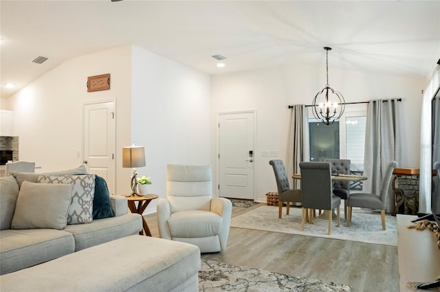 living room with visible vents, light wood finished floors, a chandelier, and vaulted ceiling