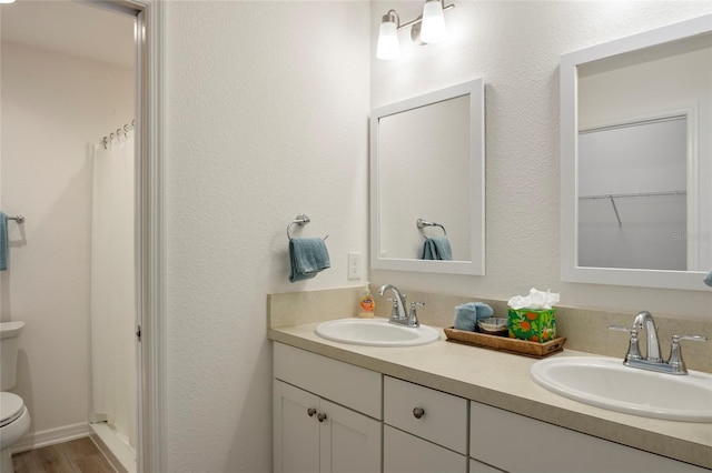 bathroom featuring a sink, toilet, wood finished floors, and double vanity