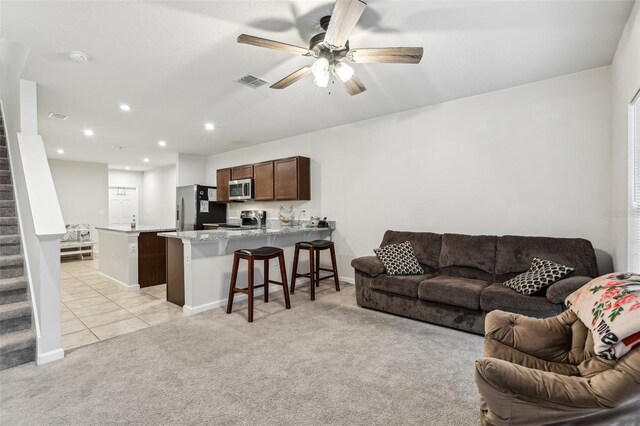 255 Blueberry Ln, Davenport, FL 33837 - living room featuring visible vents, light tile patterned floors, light colored carpet, stairs, and ceiling fan