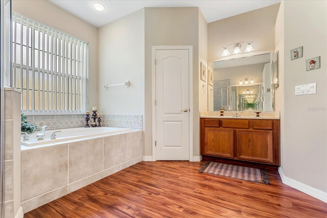 bathroom featuring a stall shower, vanity, wood finished floors, baseboards, and a bath