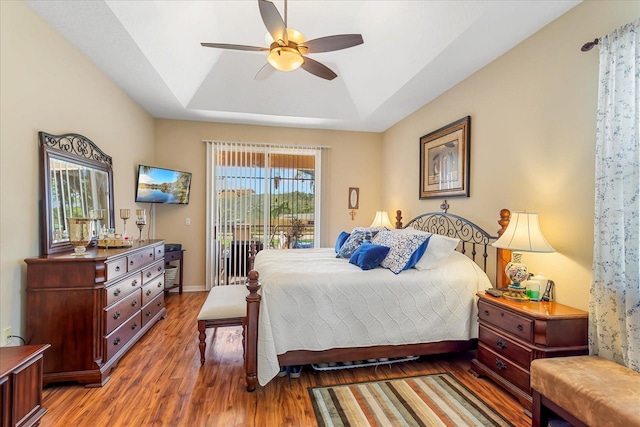 bedroom featuring access to exterior, a raised ceiling, a ceiling fan, wood finished floors, and baseboards