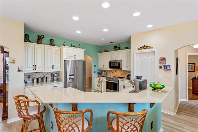 kitchen with arched walkways, stainless steel appliances, light countertops, light wood-type flooring, and a kitchen breakfast bar