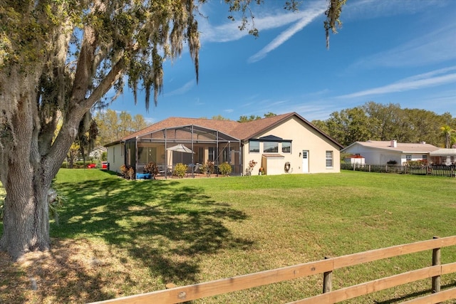 back of house featuring glass enclosure, fence, a lawn, and stucco siding